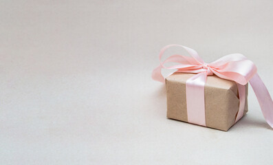 The gift, wrapped in craft and tied with a pink ribbon, is located on the craft background on the right. There is a space for text on the left. Banner. Postcard for the holiday.