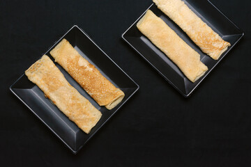 Bengali sweet - Patishapta Pitha in a black plate on isolated black background, a traditional Bengali pancake recipe where the pancakes are stuffed with kheer or coconut.