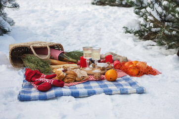 Romantic picnic setting in winter park, color blanket. Fresh food, cheese, oranges, croissants,...