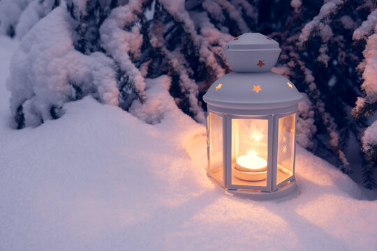 christmas lantern with a burning candle in the night forest front with a snow-covered tree
