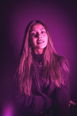 Young Caucasian model illuminated with pink neon lights. On a black wall background