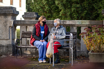 Obraz premium Senior woman with walking frame and caregiver outdoors sitting in park, coronavirus concept.
