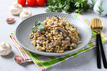 Homemade ptitim pasta with champignons in a plate on light gray table. Horizontal format.