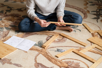Teen boy assembles furniture according to the instructions - a wooden chair. Housework and order in...