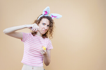 Funny angry girl in bunny ears, striped pink t-shirt is boxing with eggs. Young curly woman is preparing for celebration. Happy easter spring concept. Carnival, seasonal party decor for holiday.