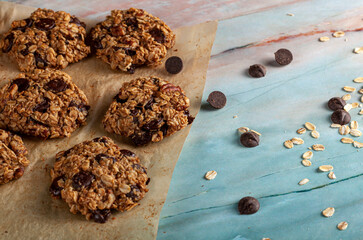 Fresh out of oven homemade cookies on baking paper of green marble countertop. Dark Chocolate chips and rolled oats are seen on the surface. A healthy fiber rich snack.