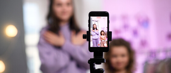 Sisters indoors at home, making video with smartphone. Lockdown concept.