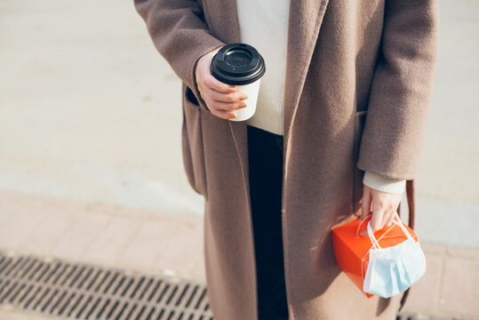 Woman In Winter Coat Is Drinking Take Away Cup Of Coffee On The Street During Covid Pandemic Restrictions, Beautiful Sunny Day. Selective Focus.