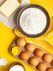 Baking ingredients for cookies, dough and pastry on yellow background. Mockup for recipe or cooking blog with eggs, flour, butter and milk. Flat lay