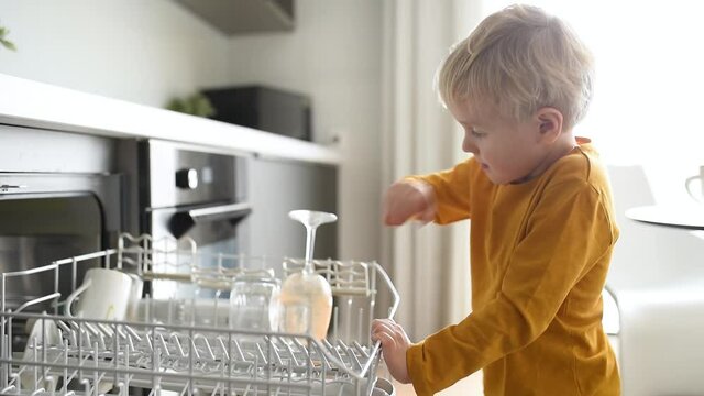 Child puts dirty crockery in the home dishwasher. Close-up. Mom's little helper.