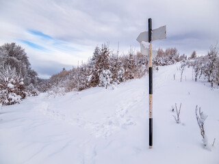 Hiking trail arrow sign at the crossroads. Winter landscape in Carpathian Mountains, Romania.