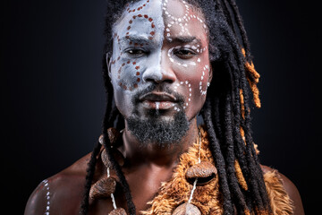 confident african aborigen isolated over black background, having colourful ethnic drawings on face