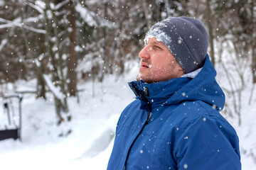 Obraz premium Portrait of a young man out in nature during snowy day in winter. Shot of a man wearing a winter coat standing in a snowy landscape. Photo of a young man with beard standing in the snowy mountains.