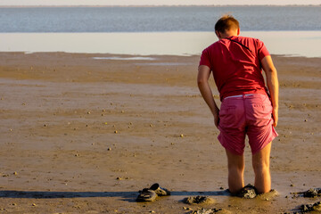 barefoot young man of the European race in a red t-shirt and pink shorts plunge in the mud