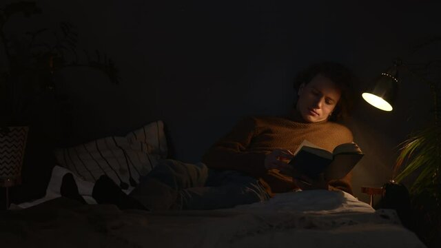 handsome guy is reading book at night lying under the lamp