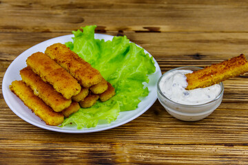 Fried fish fingers on a plate with lettuce and tartar sauce on wooden table