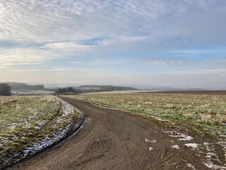 Fototapeta premium snow melting on a wide field on a sunny winters day with some clouds