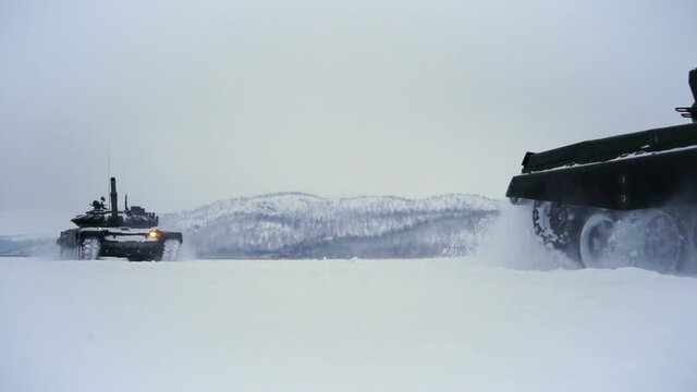 Snow-covered shooting range field on the background of the mountain. Tanks go on the field for testing