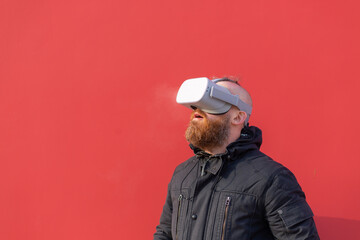 Emotional portrait of a man on the street wearing reality glasses against the background of a red wall