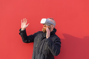 Emotional portrait of a man on the street wearing reality glasses against the background of a red wall