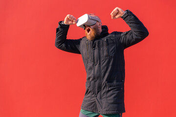 Happy contented man rejoices jumping in virtual reality glasses on wall background