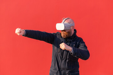 European man playing fight with virtual reality glasses on red wall background