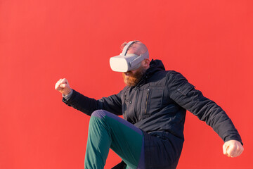 European man playing fight with virtual reality glasses on red wall background