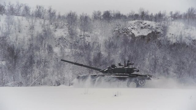Snow-covered shooting range field in the highlands. The tank rides on the field at high speed