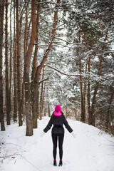 A girl in a pink scarf and hat stands in the middle of a pine forest. Beautiful pine forest on a frosty day.