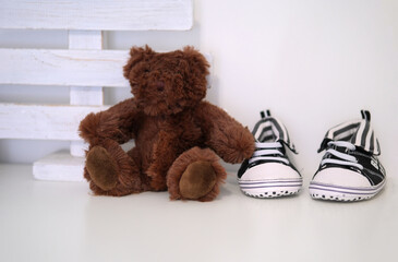 Brown teddy bear and tiny sneakers on the shelf in the nursery. Children's room interior