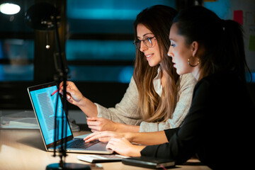 Two smart business women working together with laptop while talking in the office.