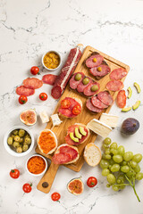 Assortment of sausages and cheese, salami camembert brie, grapes, baguette slices, olives, on white background.