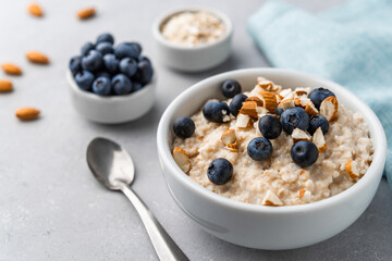 Oatmeal porridge in a bowl with blueberries and almonds on grey stone background. Concept of healthy breakfast, food, and lifestyle - obrazy, fototapety, plakaty