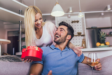 Beautiful young couple in love at home, celebrating with a gift box exchange