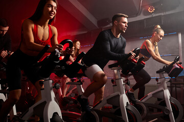 people biking in spinning class at modern gym, exercising on stationary bike. group of caucasian people athletes training on exercise bike - obrazy, fototapety, plakaty