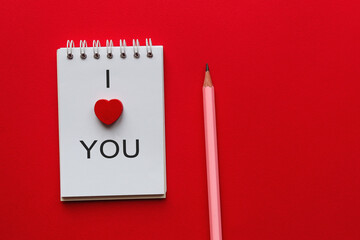 Open notebook with the inscription I love you and a pencil on a red background and copy space. Valentine's Day Concept