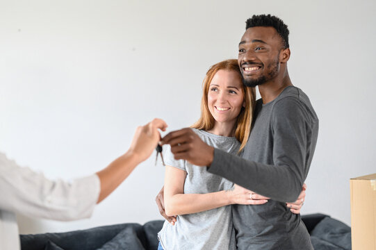 Close-up joyful newlyweds buying own apartment. Married couple take a key of new house from real estate agent. Beautiful caucasian woman and handsome african american man cuddling, enjoy togetherness
