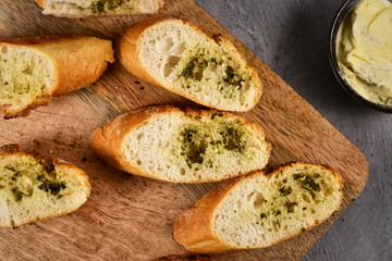 Top view of slices of baguette bread topped with melted herb butter on wooden cutting board