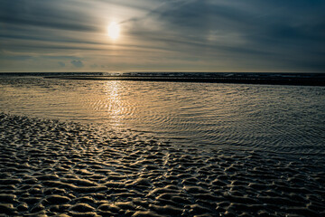 Setting sun behind sandbank at low tide at the beach