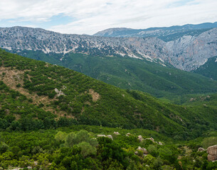 Naklejka na ściany i meble Aerial View of green forest landscape of Supramonte Mountains with limestone rock and mediterranean vegetation, Region Nuoro, Sardinia, Italy. Summer cloudy day