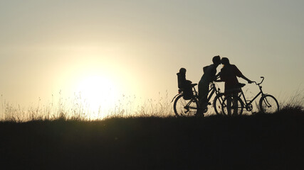 The newlyweds in love kiss with the child on the bicycles during the sunset.