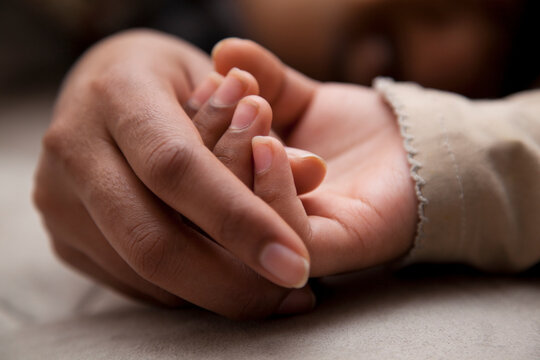 Little girl holding mom's hand as she sleeps
