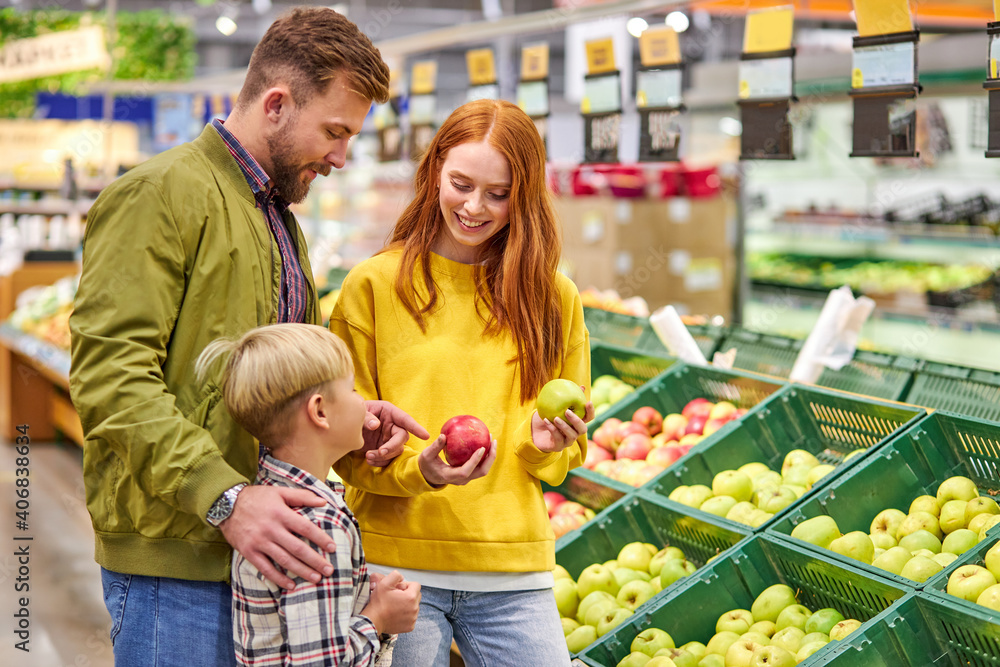 Wall mural husband and wife with a kid buy fruits, apples. family of three choosing fresh apple in fruits depar