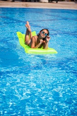 Young sexy wman in a swimsuit swims in the pool on an inflatable mattress. Girl in sunglasses in a blue pool on vacation