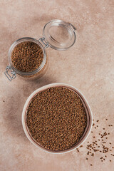 Bowl of dry raw buckwheat groats and glass jar on a light beige background. Cooking buckwheat porridge concept.