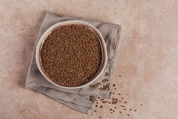 Bowl of dry raw buckwheat groats on a light beige background. Cooking buckwheat porridge concept.