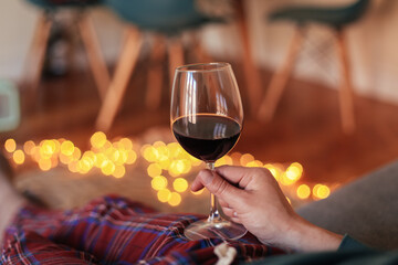 Man holding a glass of red wine, sitting on a couch in a cosy room, in red check pajamas