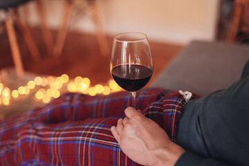 Man holding a glass of red wine, wearing сщын pajamas, sitting at home