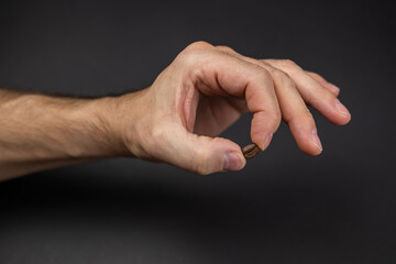 a mans hand holding a coffee bean above a dark colored table