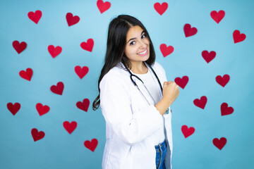 Young doctor woman wearing medical coat and stethoscope over blue background with red hearts feeling happy, positive and successful, motivated when facing a challenge or celebrating good results